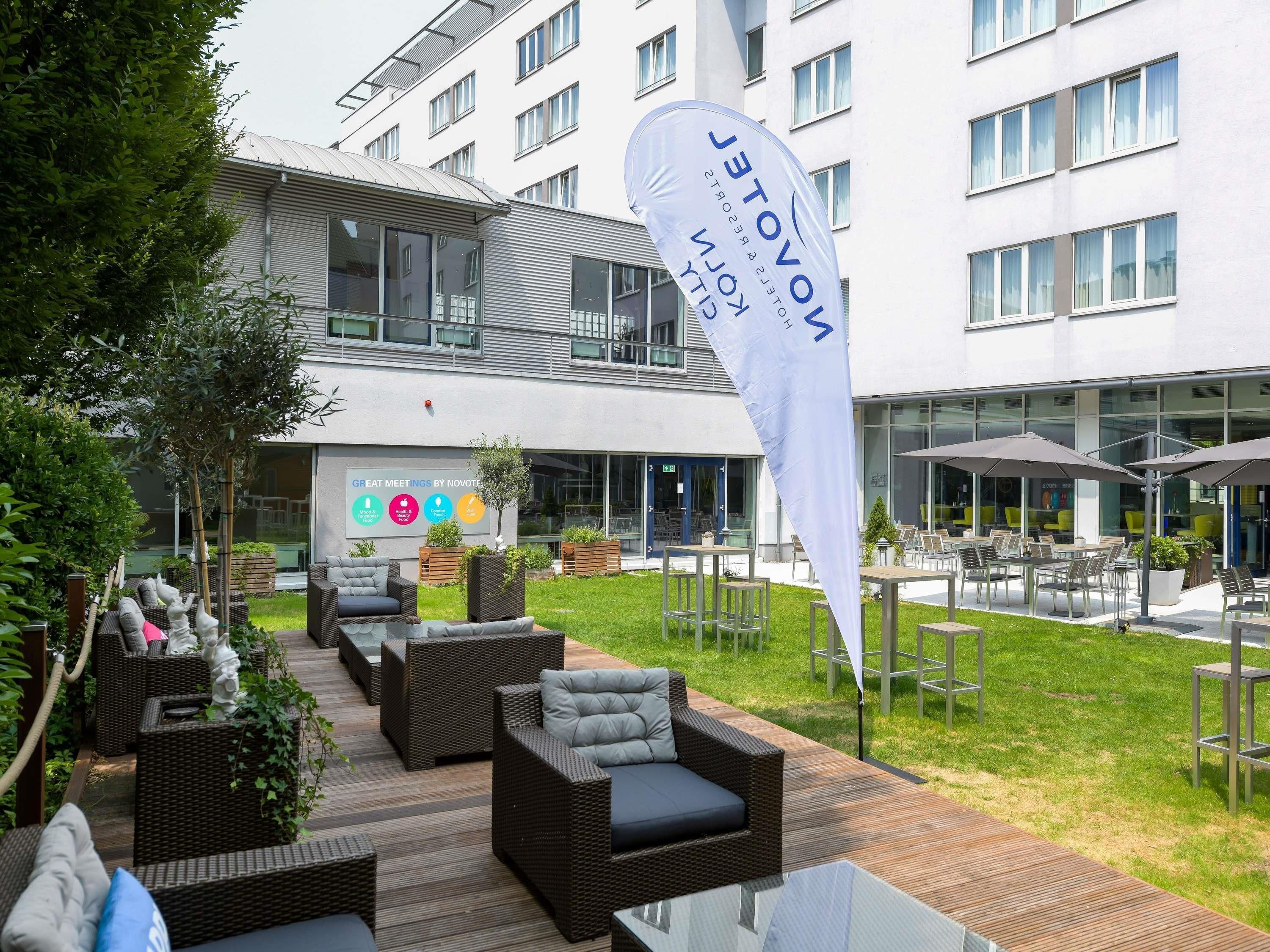 An outdoor seating area with wicker furniture, a flag, and a building with large windows and a sign.