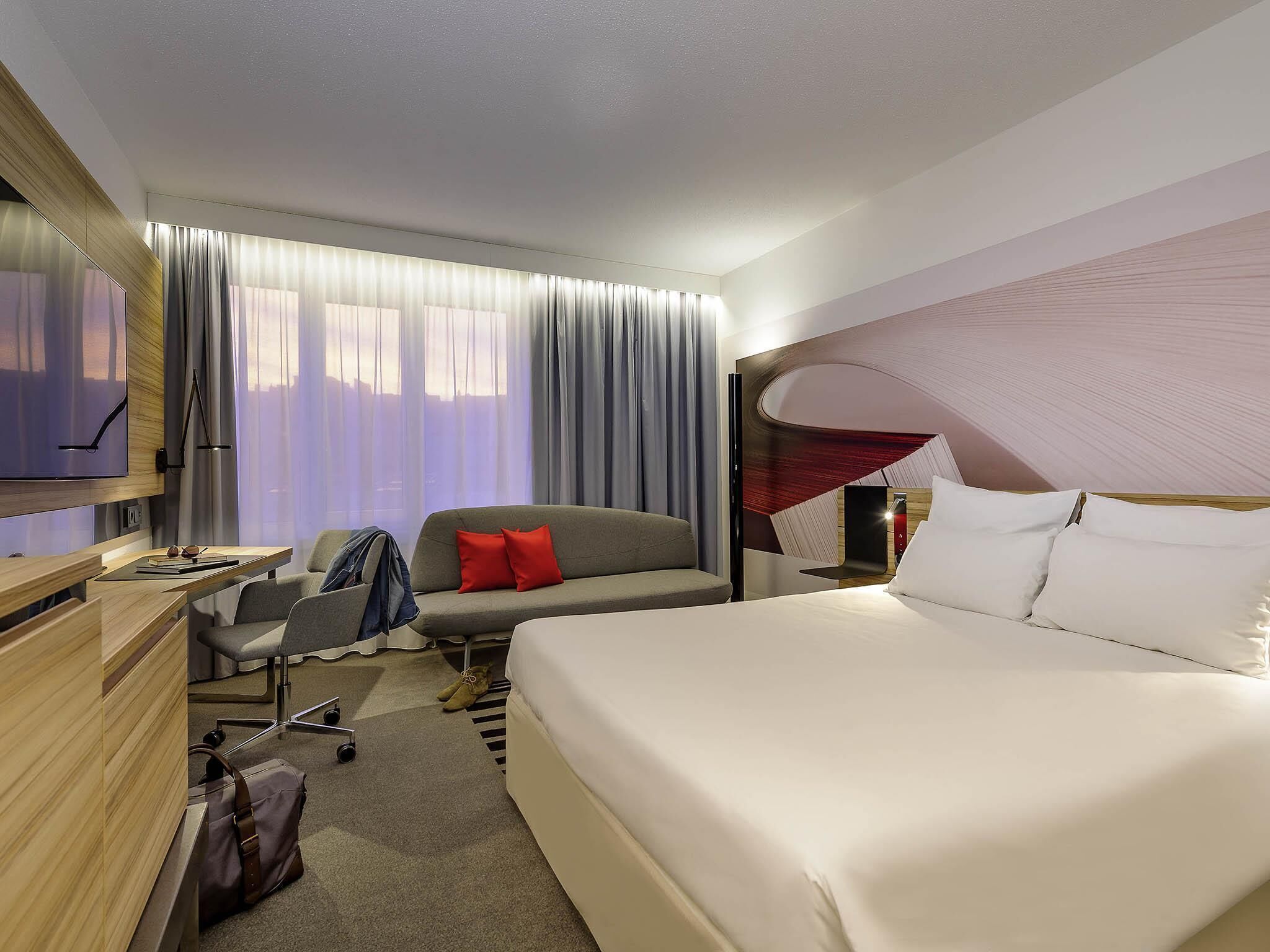 A hotel room with a bed, a desk, a chair, a TV, and a window with curtains.
