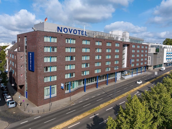 Un hôtel à plusieurs étages, reconnaissable à son grand panneau « NOVOTEL », à sa façade en briques et à son architecture moderne.