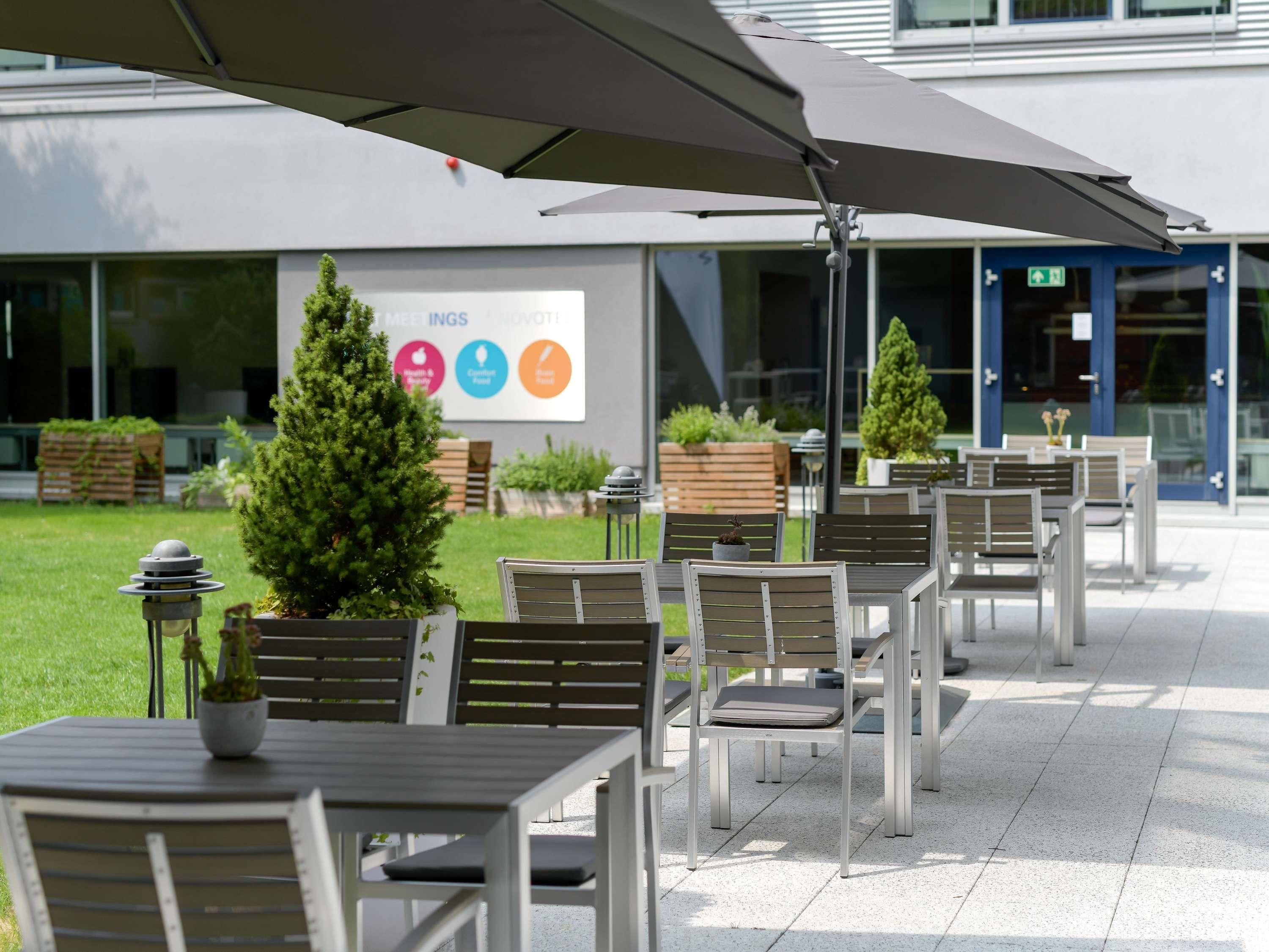 Outdoor seating with tables and chairs, a large umbrella, and a sign with icons indicating amenities.