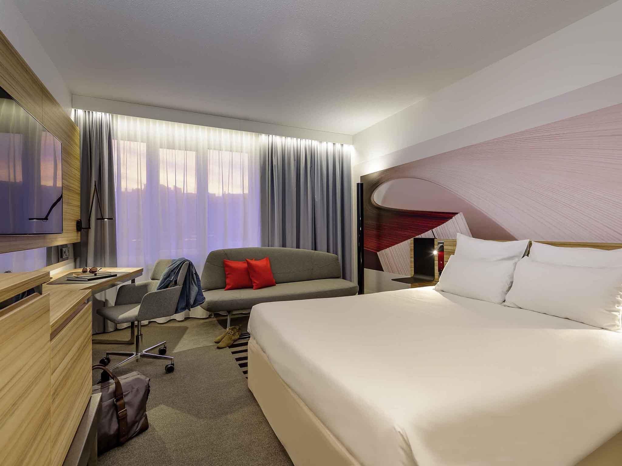 A hotel room with a bed, a desk, a chair, a TV, and a window with curtains.