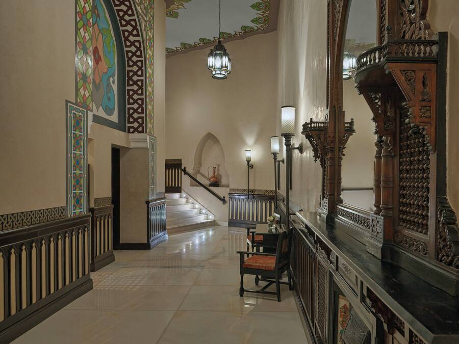 Una majestuosa escalera con barandillas ornamentales, un candelabro y un espejo grande con tallas detalladas.