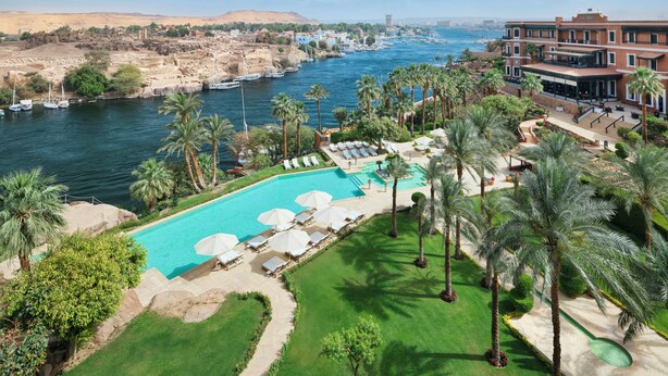 Ein Resort mit Schwimmbad, Palmen und Blick auf einen Fluss mit Booten.