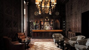 Eine Bar mit einer Holztheke, mehreren Stühlen, einem gemusterten Teppich und einer Kristallleuchter.