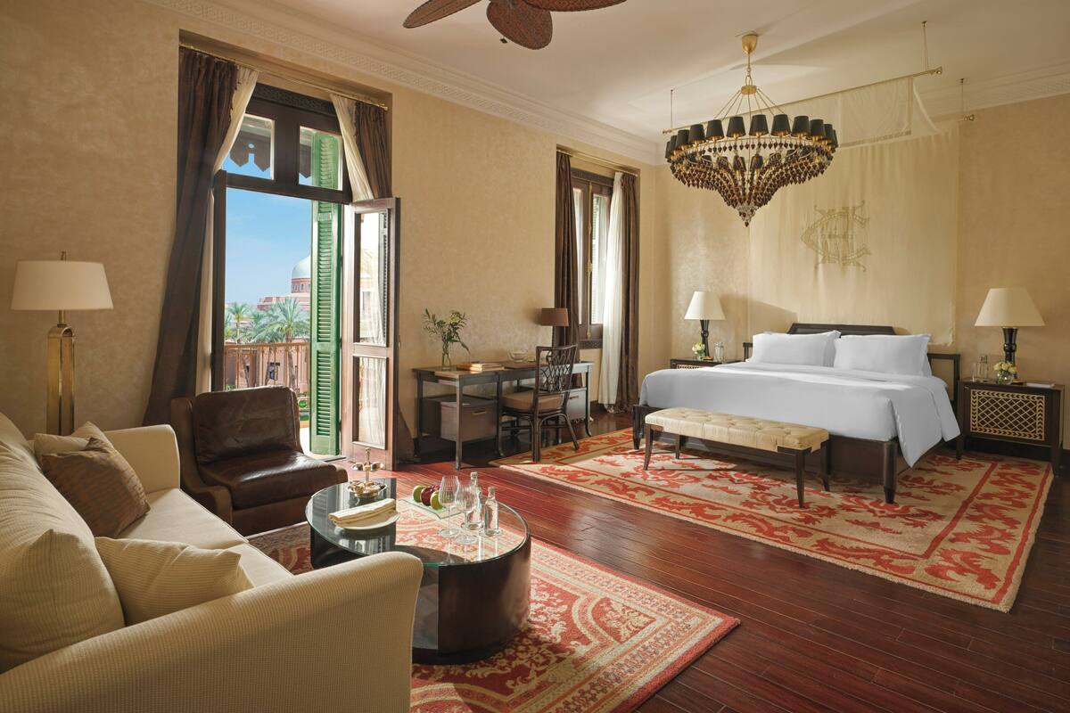 A hotel room with a bed, a desk, a chair, a sofa, a coffee table, and a chandelier.