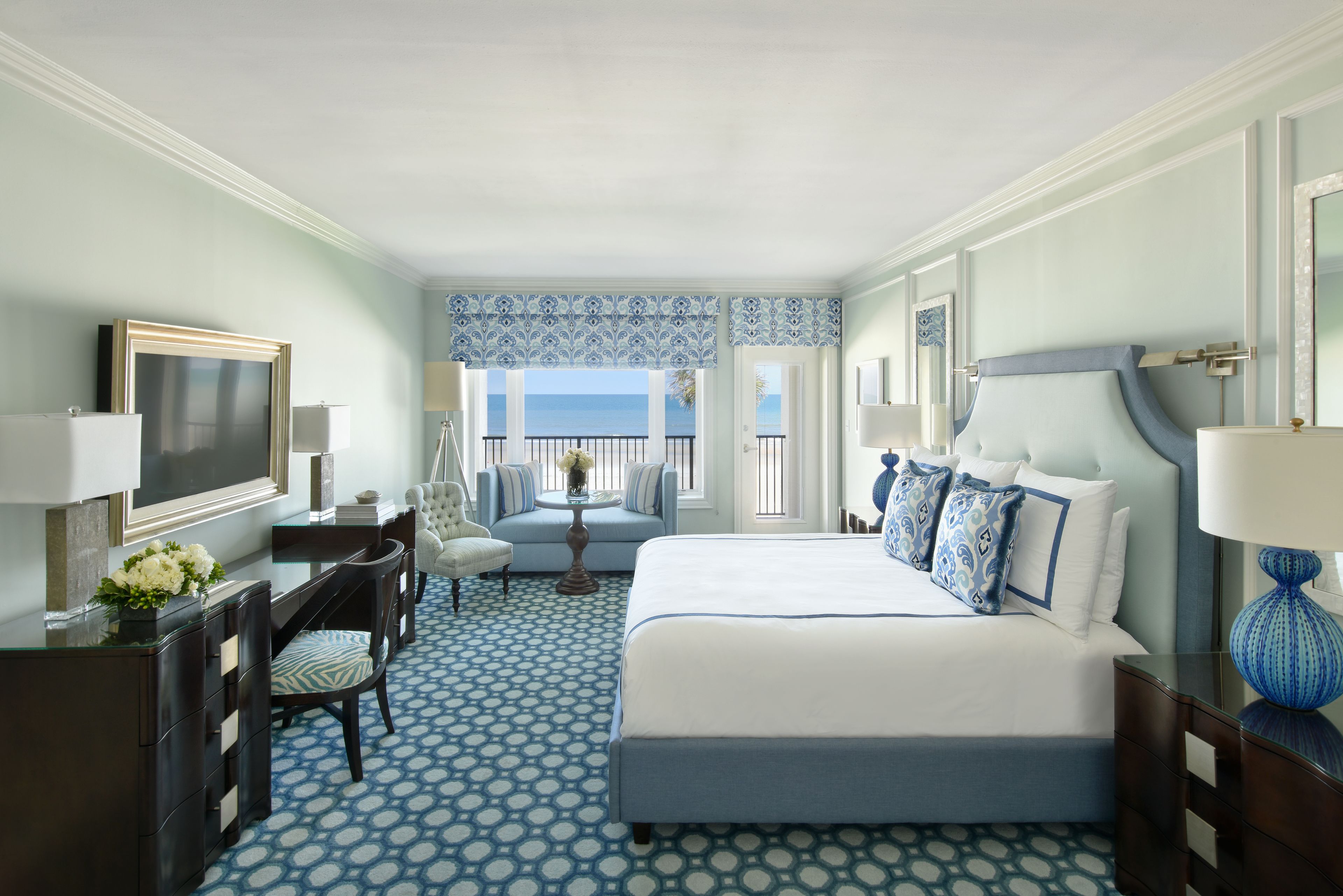 A hotel room with a large bed, a desk, a chair, and a view of the ocean.