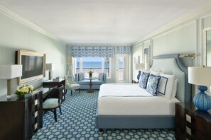 A hotel room with a large bed, a desk, a chair, and a view of the ocean.
