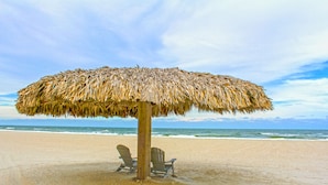 A beach umbrella with two chairs underneath, a sandy beach, and the ocean in the background. - Ponte Vedra Inn & Club (Ponte Vedra Beach)