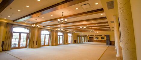 A spacious hall with high ceilings, chandeliers, and large windows.