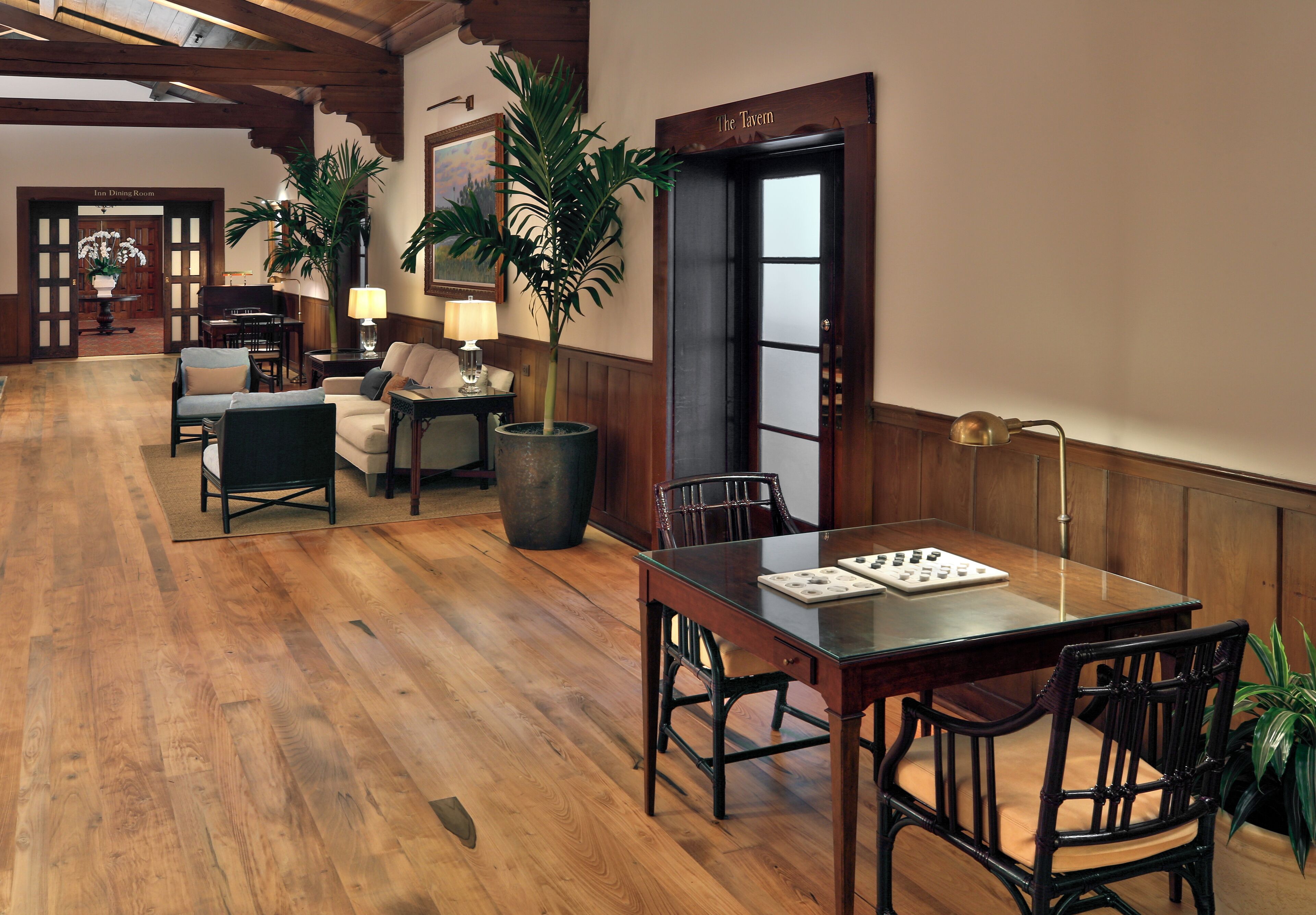 Een ruime lobby met een houten vloer, een eettafel met stoelen, een bank en een grote potplant.