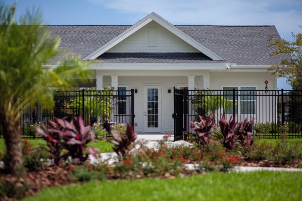 A white house with a grey roof, a black metal fence, and a garden with various plants and flowers.