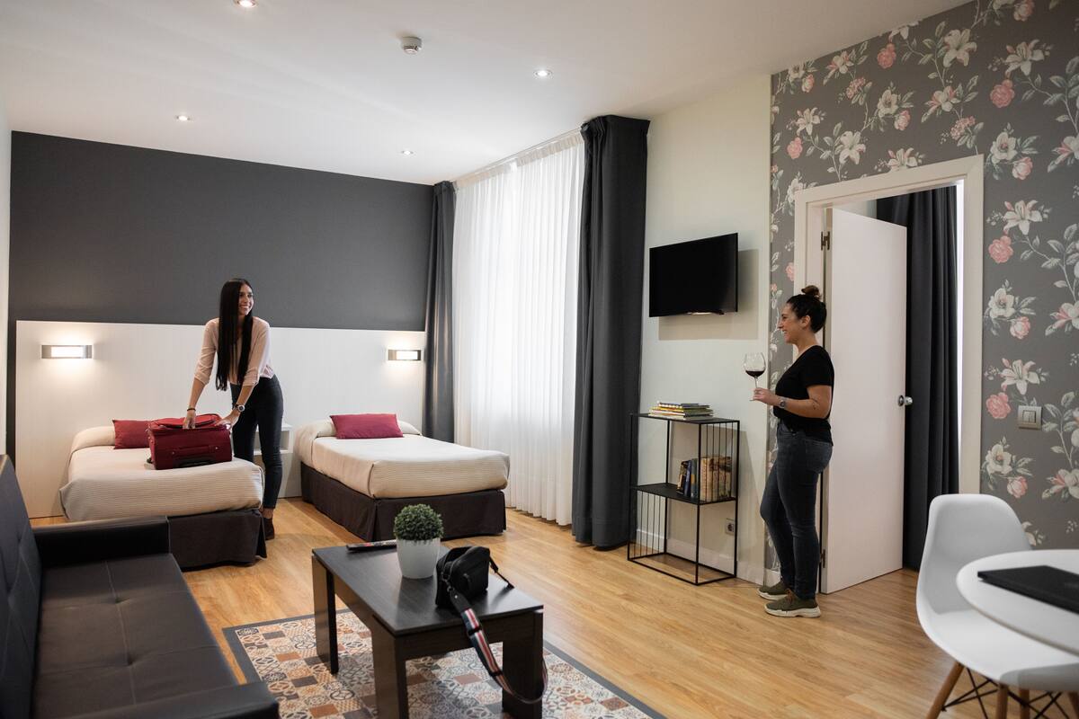 Quarto de hotel moderno com duas camas, um sofá, uma mesa de centro e uma televisão.