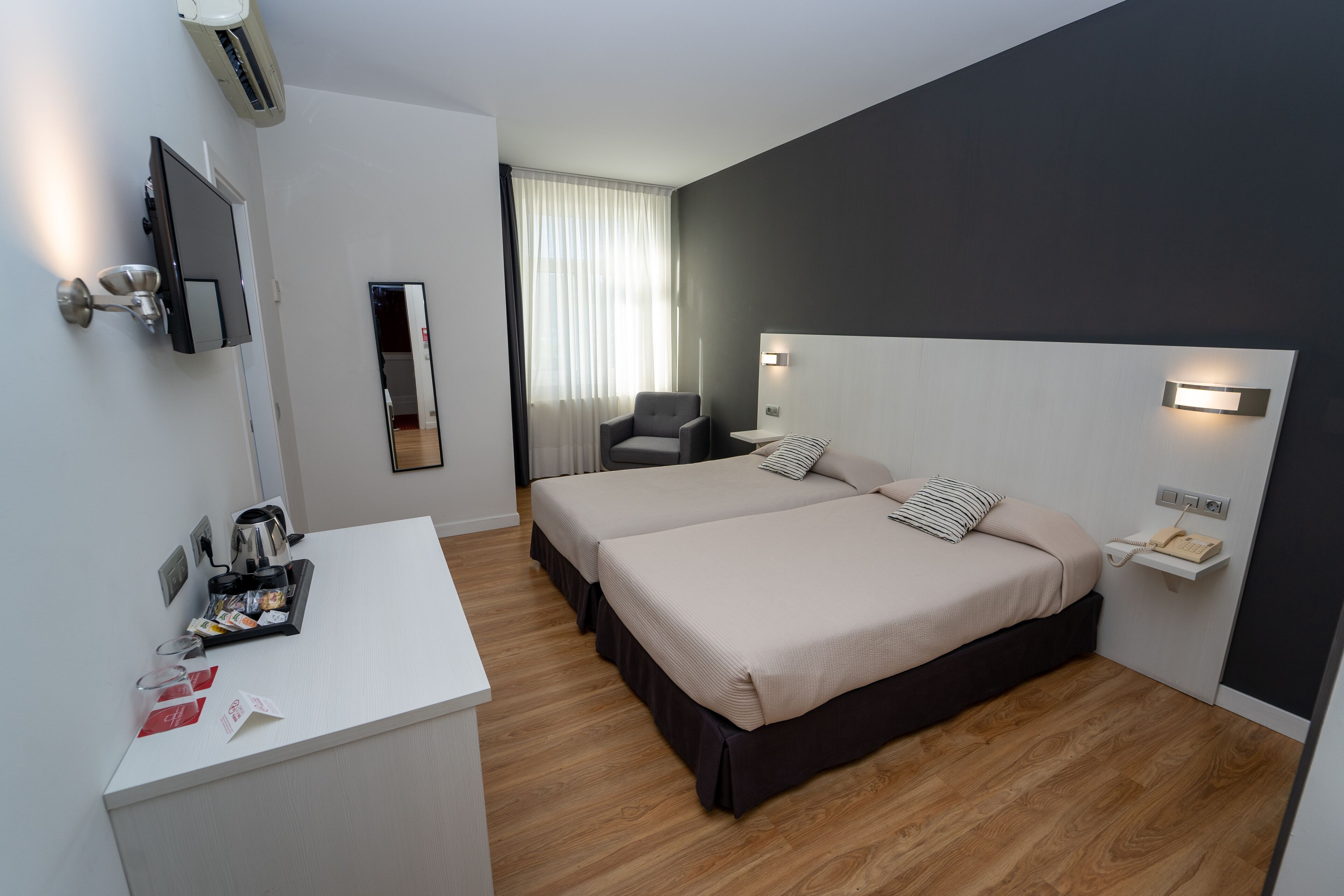 A hotel room with two beds, a desk, a chair, a TV, and a bedside table with a phone.