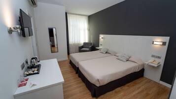 A hotel room with two beds, a desk, a chair, a TV, and a bedside table with a phone.