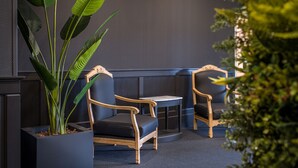 Un área de estar con dos sillas de madera y una mesita pequeña, rodeada de plantas grandes en macetas.