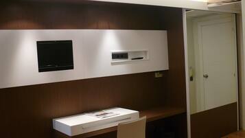 Una habitación pequeña y privada con escritorio, silla y televisión fijada a la pared.