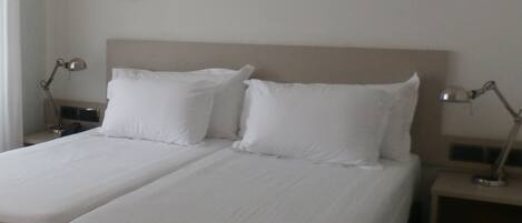 Una cama doble con sábanas blancas y dos lámparas de noche.
