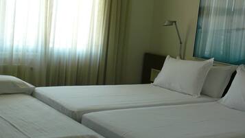 A hotel room with two beds, a nightstand, a lamp, and a window with curtains.