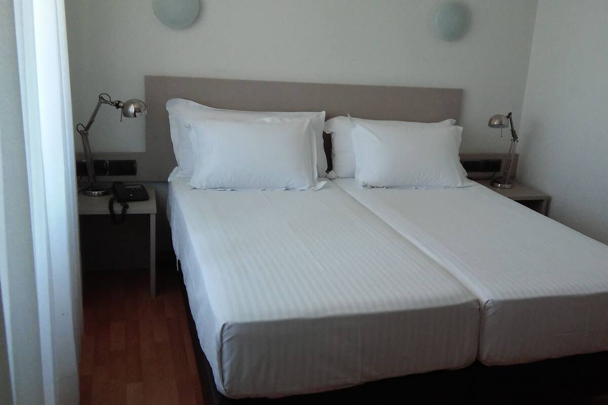 A double bed with white linens, two bedside tables with lamps, and a wooden floor.