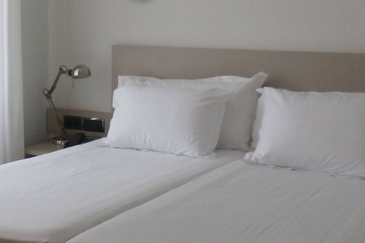 A double bed with white linens and two bedside lamps.