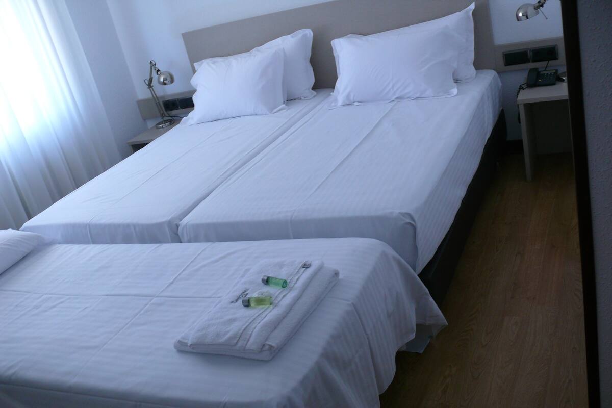 A hotel room with two single beds, a nightstand with a lamp, and a small table with a phone.