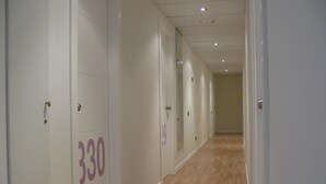 Corredor com portas numeradas, paredes claras e soalho de madeira.