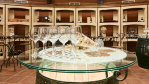 Zona de bar con una mesa redonda de vidrio que muestra copas y botellas de vino, rodeada de estantes llenos de botellas.