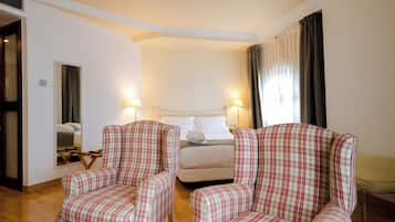 Una habitación de hotel con una cama, dos sillones a cuadros, una mesita de noche y un espejo.