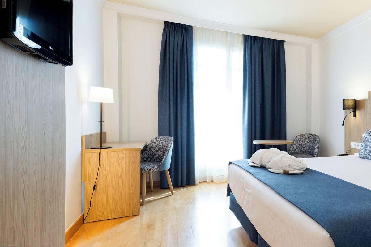Une chambre d’hôtel moderne équipée d’un grand lit, d’un bureau, d’une chaise et d’un téléviseur.
