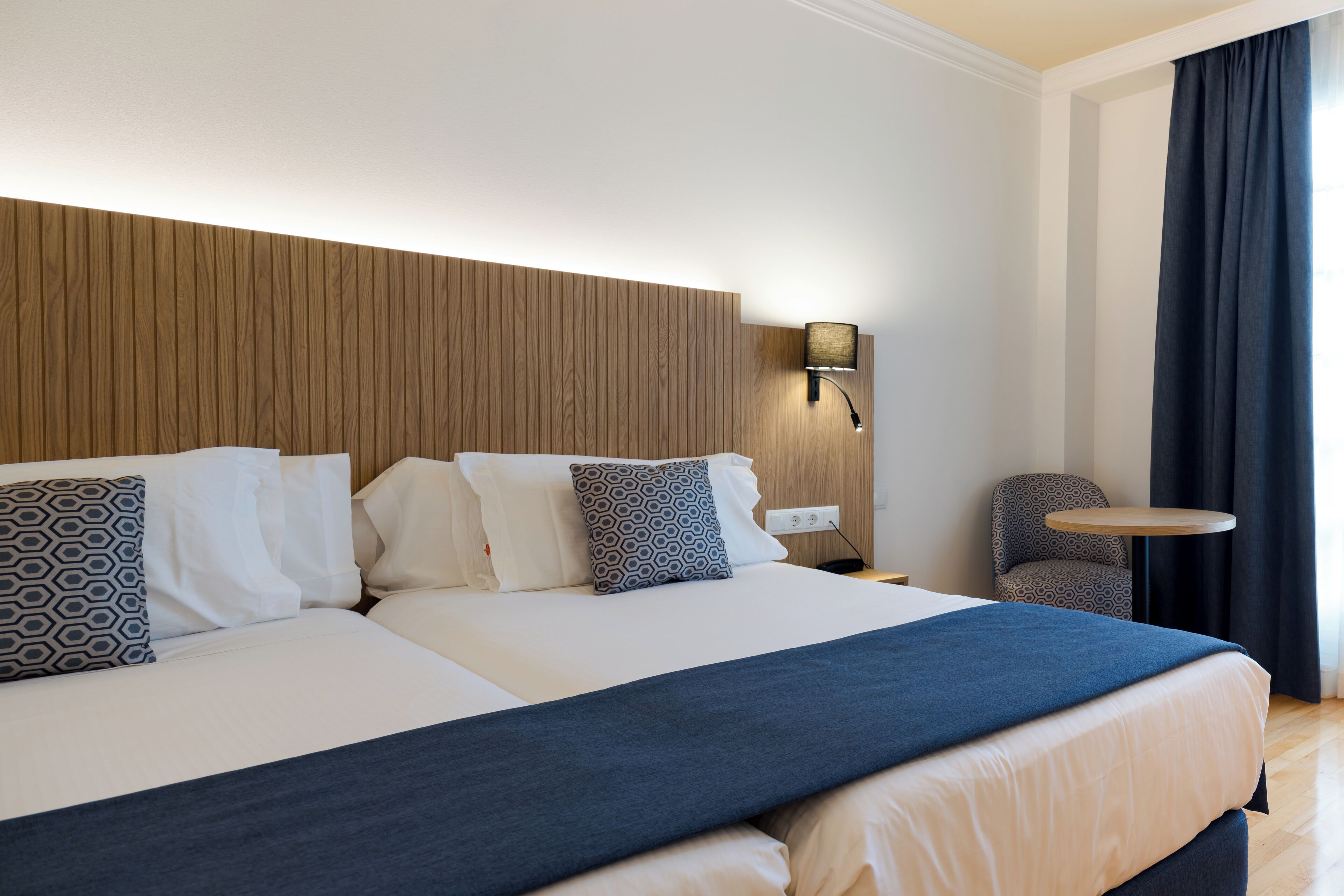 Una habitación de hotel con una cama grande, una mesita de noche, una lámpara y una silla.