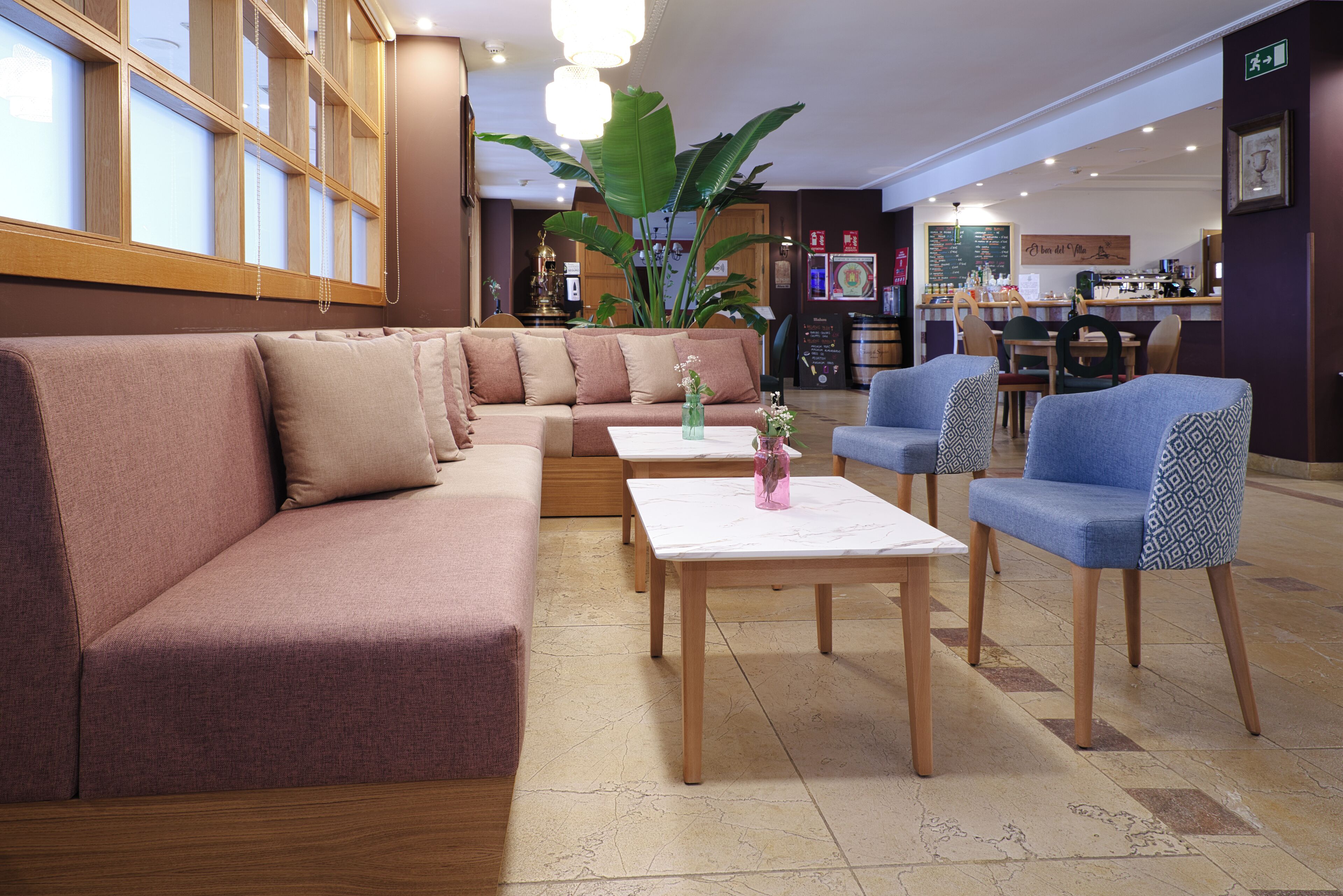 Un hall d’hôtel avec un canapé, des fauteuils, une table basse et une grande plante.