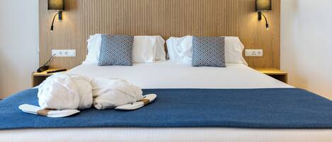 A neatly made bed with white linens, two patterned pillows, a blue throw blanket, and a white robe on the bed. There are two bedside tables with lamps and a power outlet on each.
