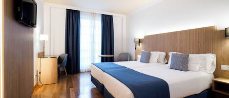 A hotel room with a large bed, a desk with a chair, a TV, and a bedside table.
