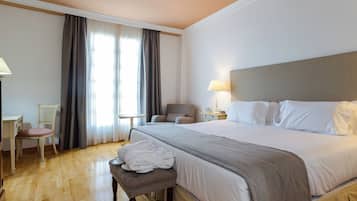 Una habitación de hotel con una cama grande, lámparas de noche, un armario de madera, una silla y un banco.