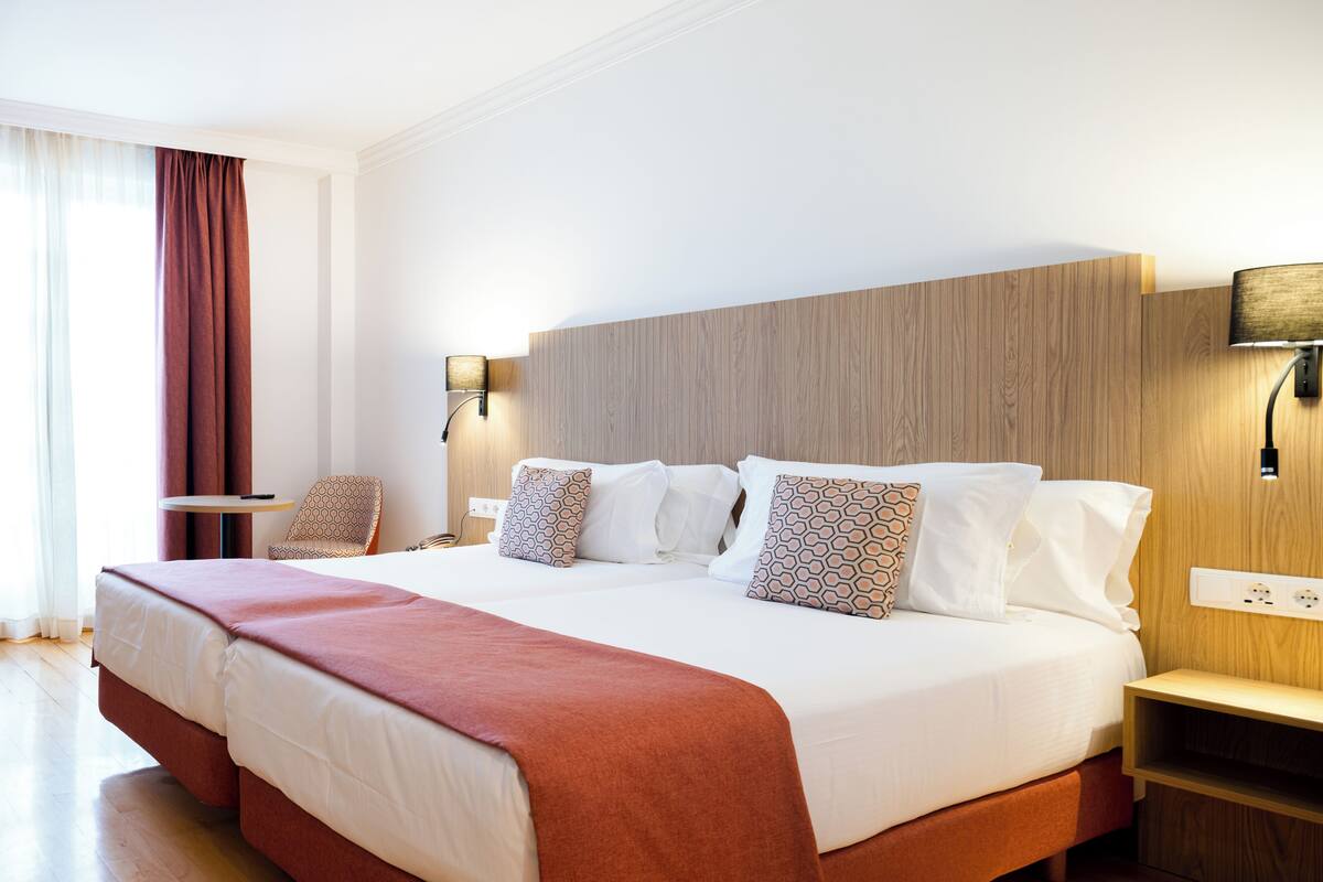 Une chambre d’hôtel avec un grand lit, deux tables de chevet, une chaise et une fenêtre avec des rideaux.