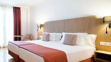 Una habitación de hotel con una cama grande, dos mesitas de noche, una silla y una ventana con cortinas.
