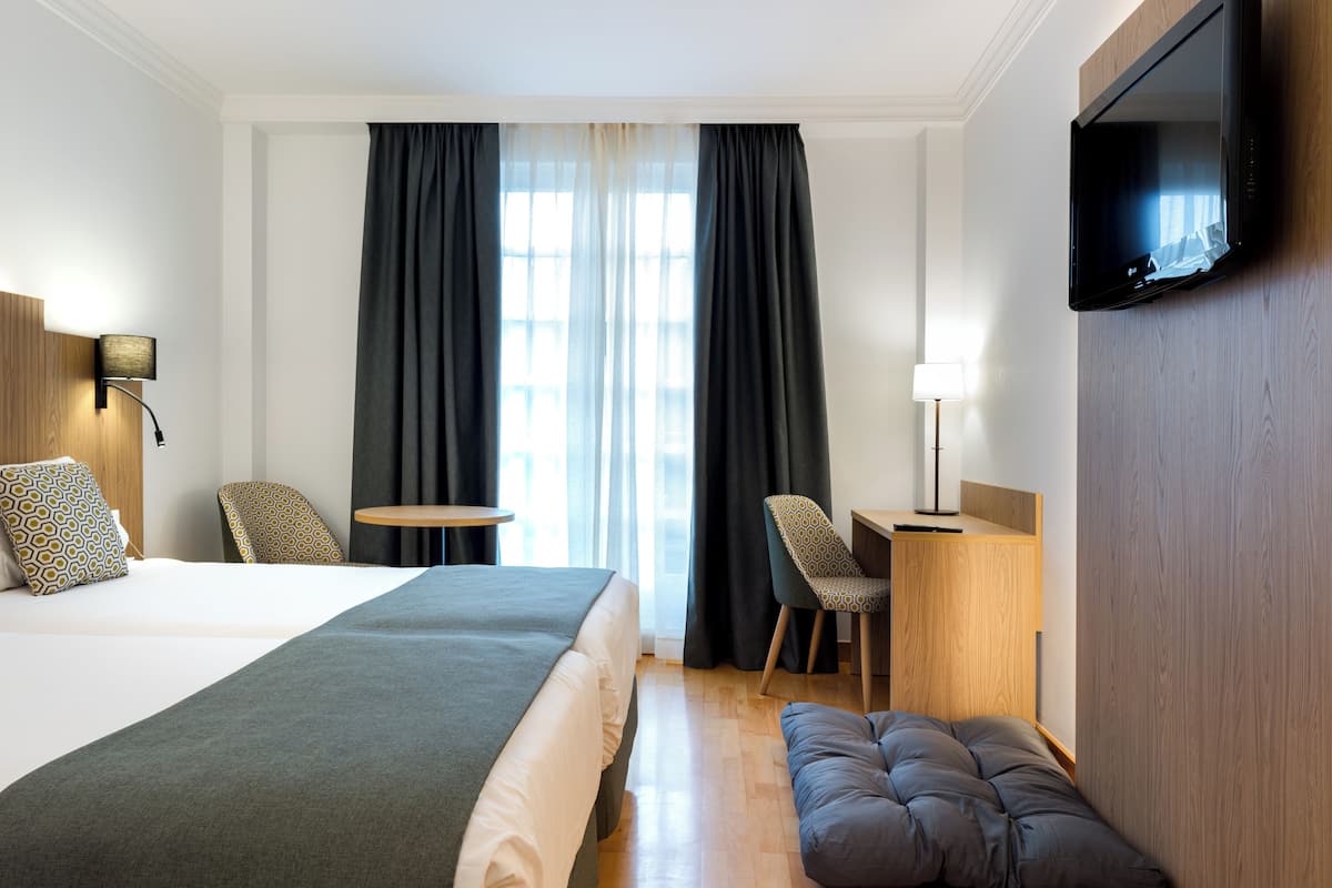 Une chambre d’hôtel avec un grand lit, un bureau, une chaise, une télévision et une fenêtre avec des rideaux.