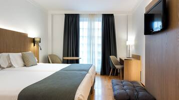 A hotel room with a large bed, a desk, a chair, a TV, and a window with curtains.