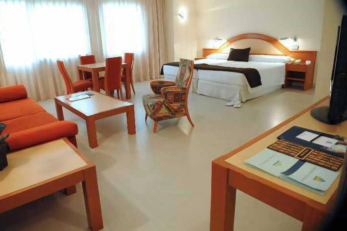 A hotel room with a bed, a desk, a chair, a sofa, and a TV.
