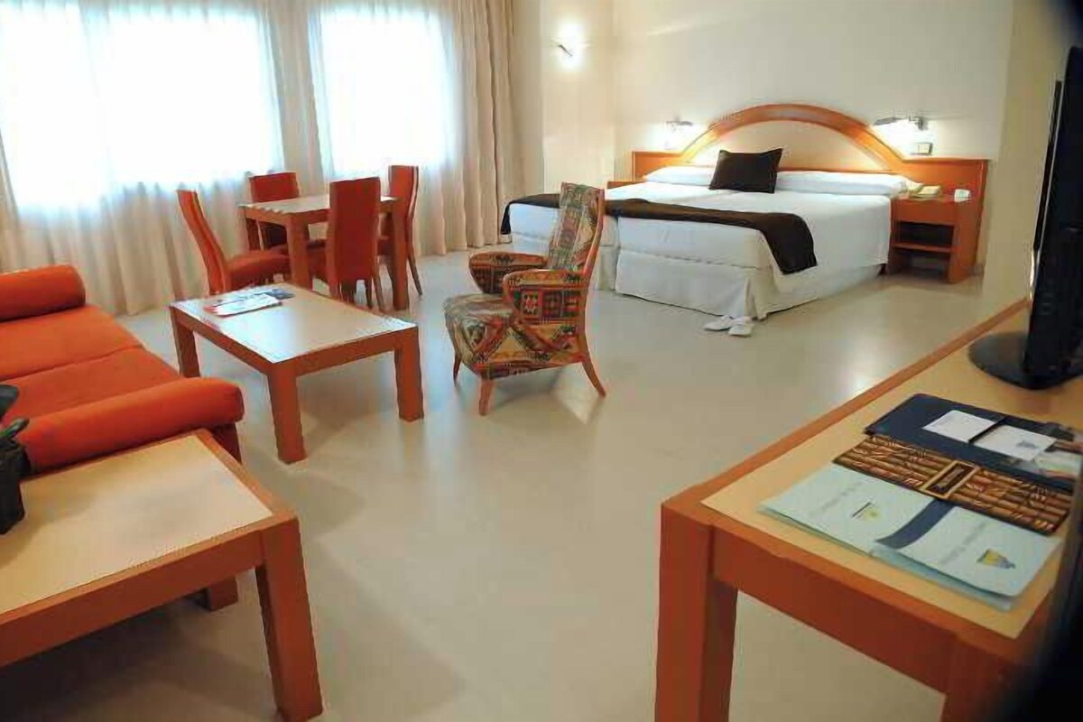 A hotel room with a bed, a desk, a chair, a sofa, and a TV.