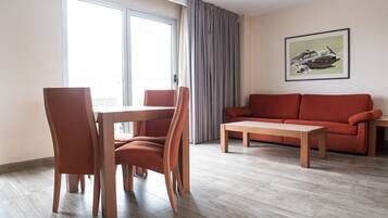 Una sala de estar moderna con una mesa de comedor y sillas, un sofá, y un ventanal con cortinas.