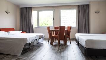 A hotel room with two single beds, a dining table with chairs, and large windows with curtains.