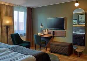 Una habitación de hotel con cama, un escritorio con silla, teléfono y un espejo grande.