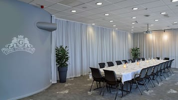 Un salón de conferencias con una larga mesa, sillas y plantas en macetas.