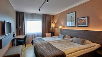Une chambre d’hôtel avec un grand lit, un bureau avec une chaise, une télévision et deux tableaux encadrés au mur.