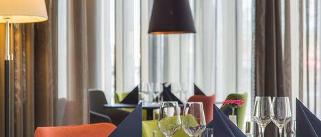 A restaurant setting with a table set for two, featuring a dark-colored tablecloth, two wine glasses, and a small vase with a pink flower.