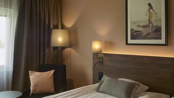 A hotel room with a bed, a chair, a lamp, and a framed picture on the wall.