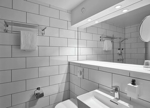 Un baño moderno con azulejos blancos, un lavabo, un espejo y una ducha.