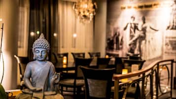 A Buddha statue in a dimly lit room with a chandelier, tables, and chairs.
