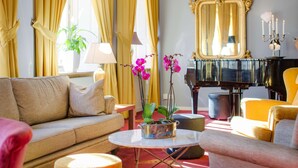 A living room with a sofa, armchairs, a piano, and a vase with flowers.